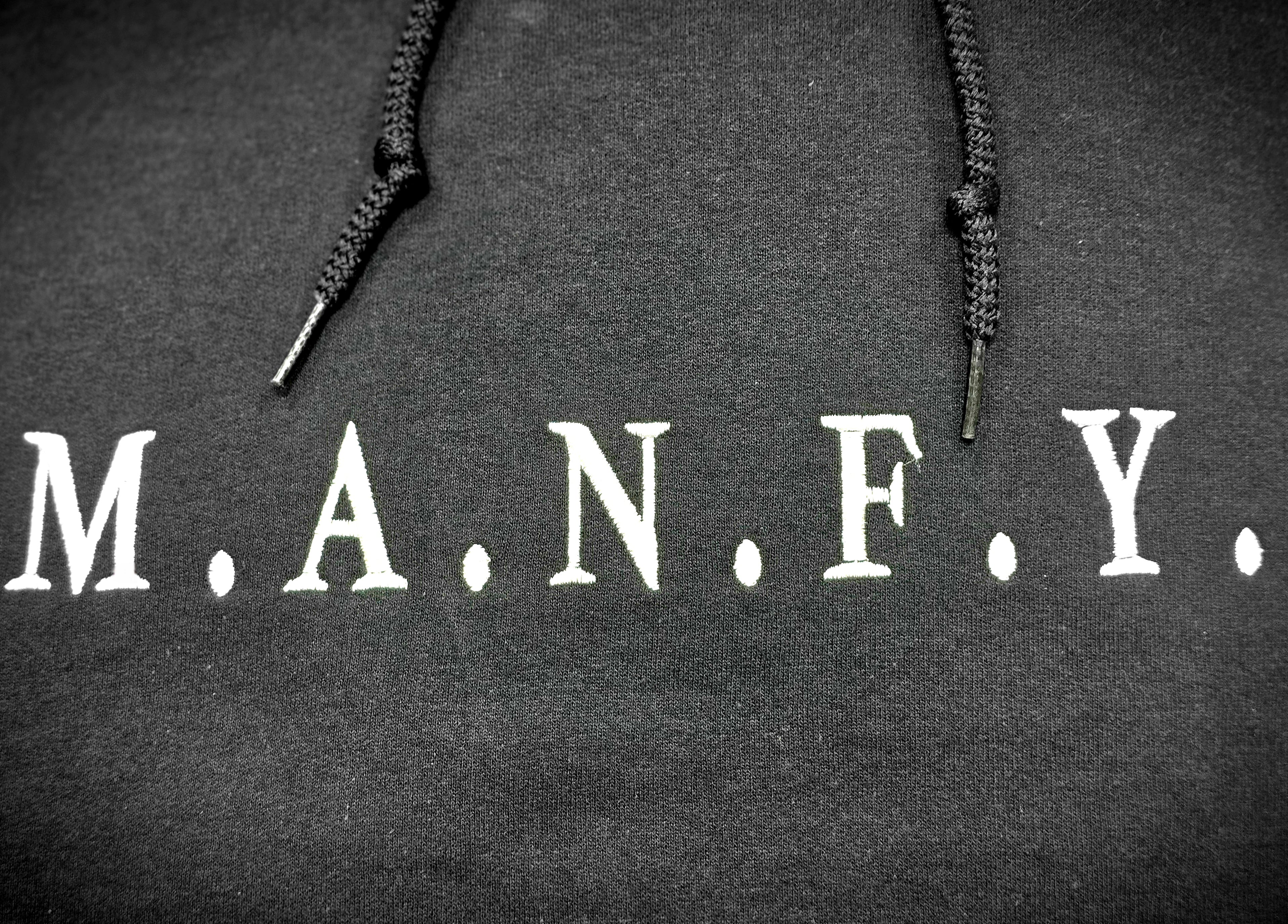 Close-up of premium white M.A.N.F.Y. embroidery stitched on black hoodie fabric