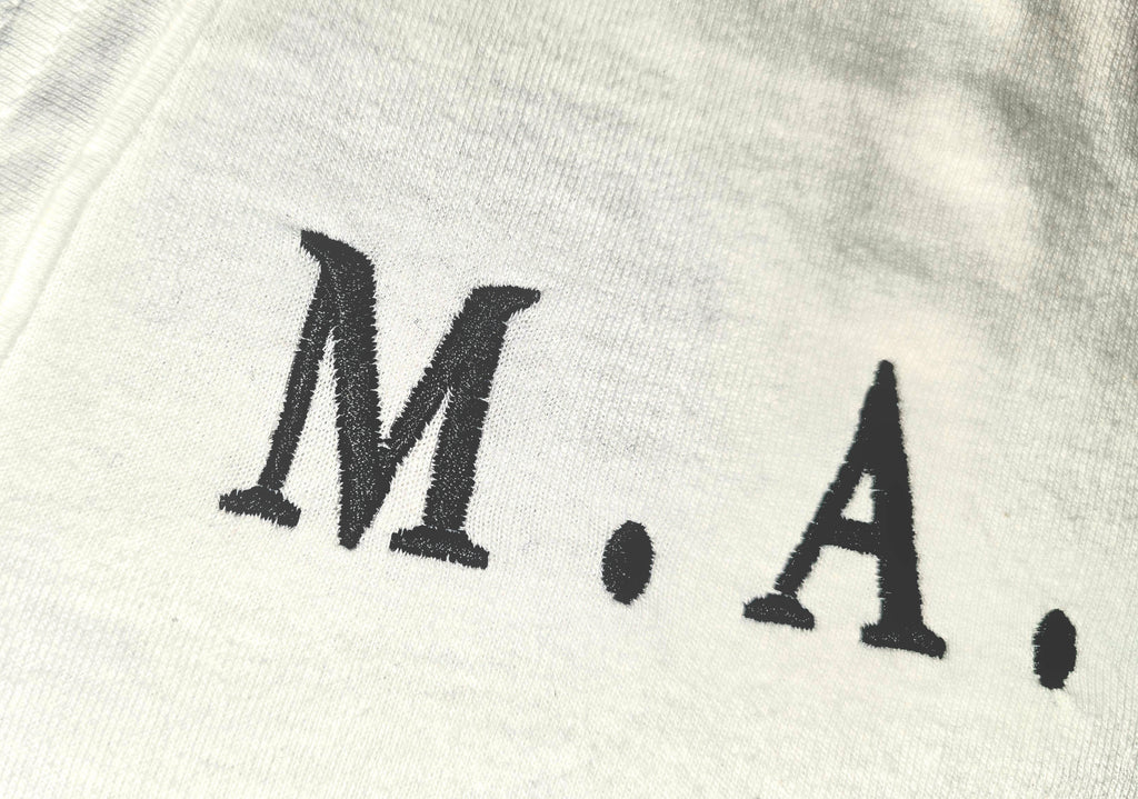 Close-up of black M.A.N.F.Y. logo on white tee fabric